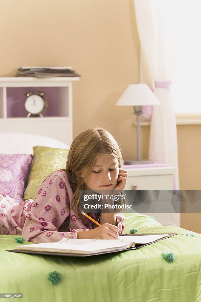 Teenage lifestyle shot of a girl in pink pajamas as she does her homework on her bed