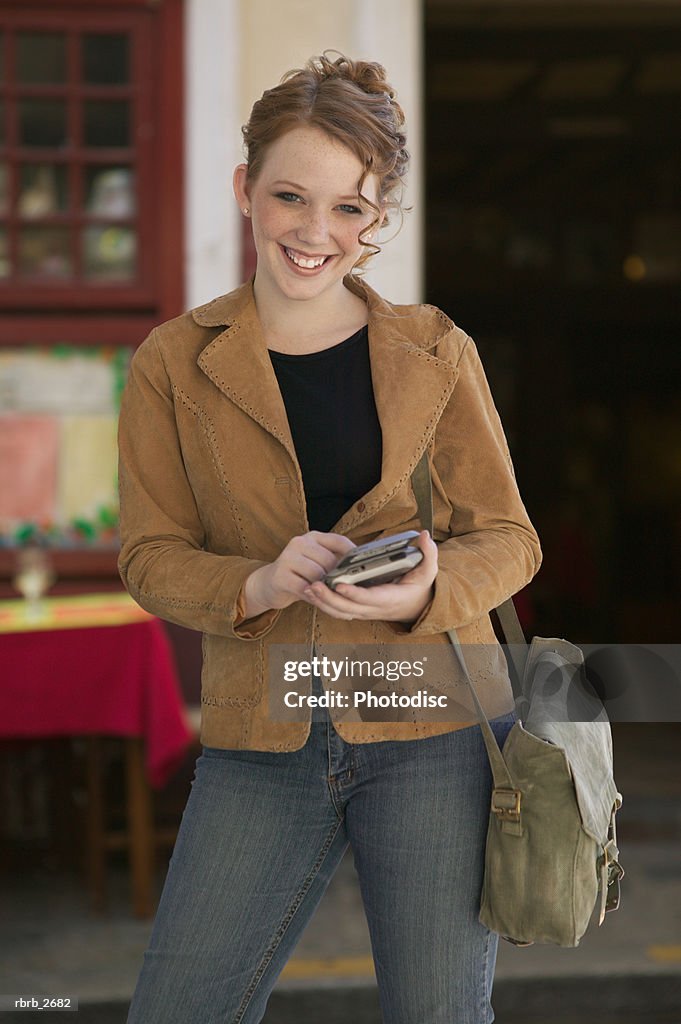 Teenage lifestyle shot of a redheaded female in a brown jacket as she stands using an electronic planner