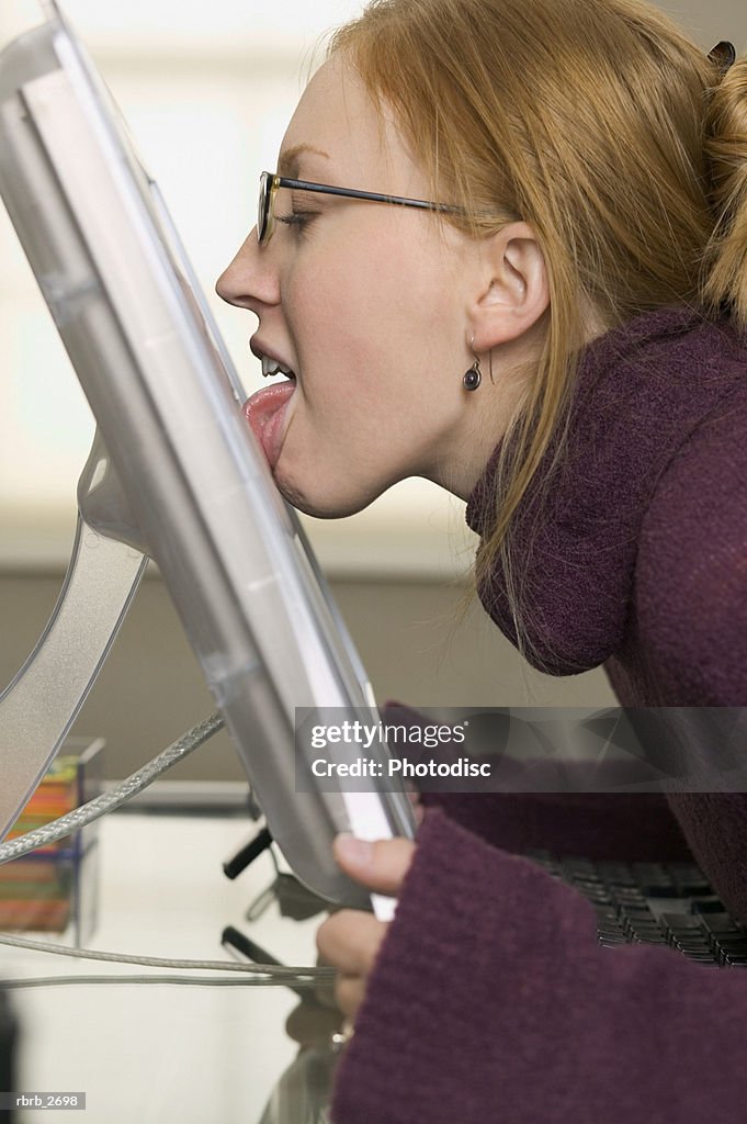 Conceptual shot of a young adult female as she licks her computer screen