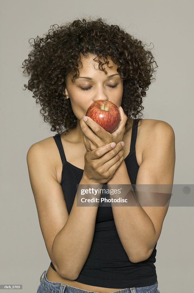 Beauty portrait of young adult female in a black tank top as she bites into an apple