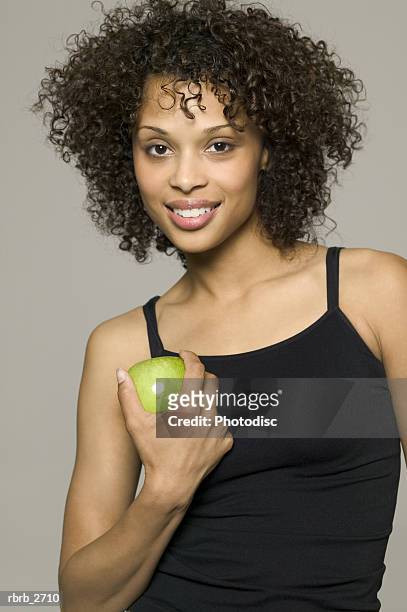 beauty portrait of young adult female in a black tank top as she holds a green apple - taste of john paul ataker presentation spring 2016 new york fashion week stockfoto's en -beelden