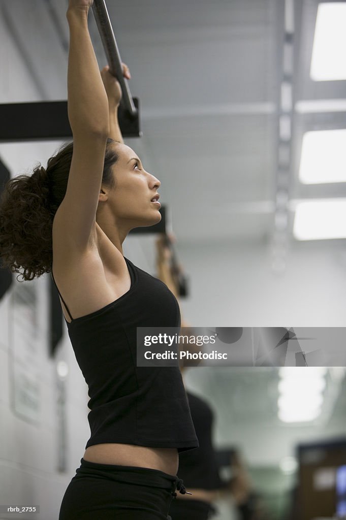 Fitness lifestyle shot of a young adult woman in a workout outfit as she does pull ups