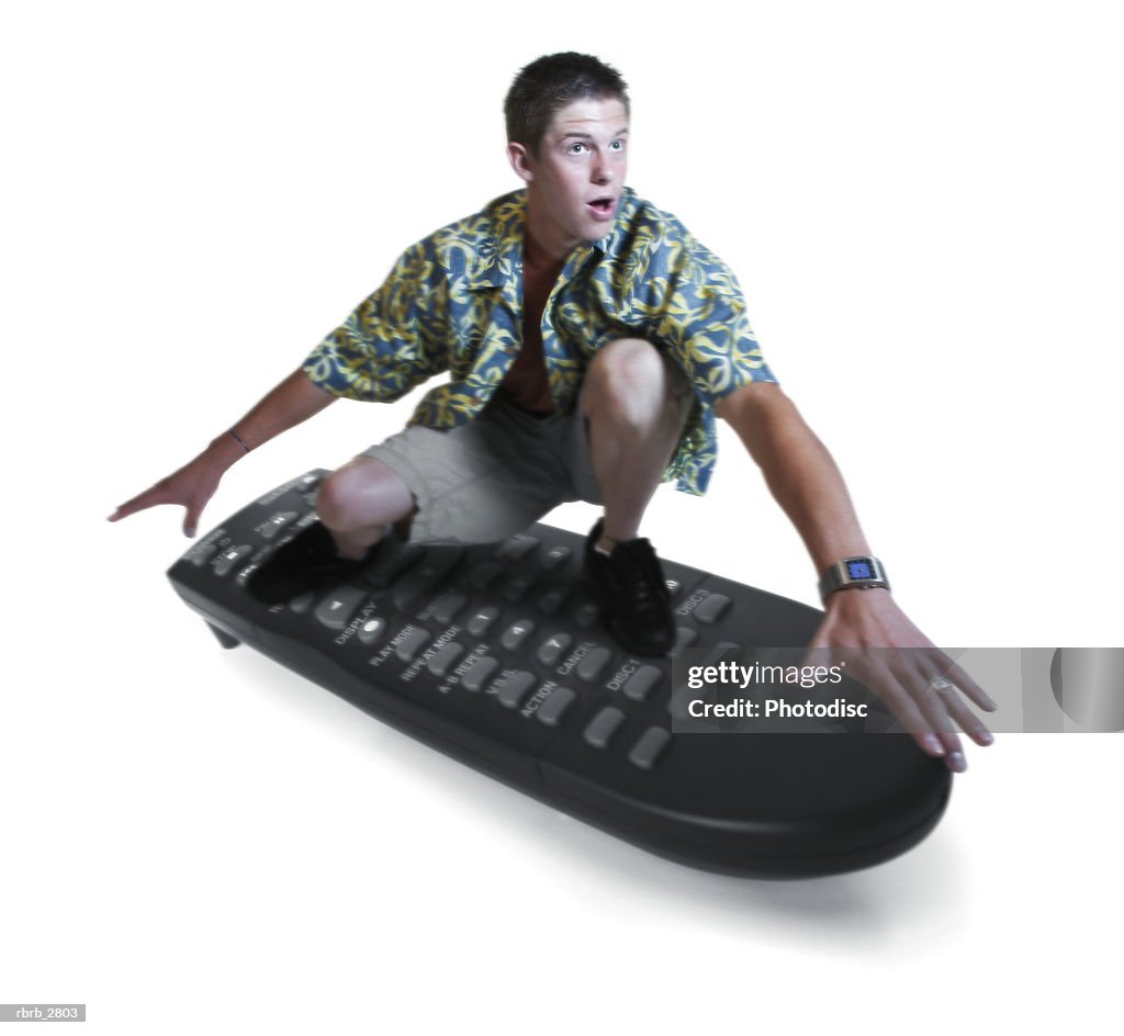 Conceptual shot of a teenage male in a hawaiian shirt as he surfs on a tv remote control