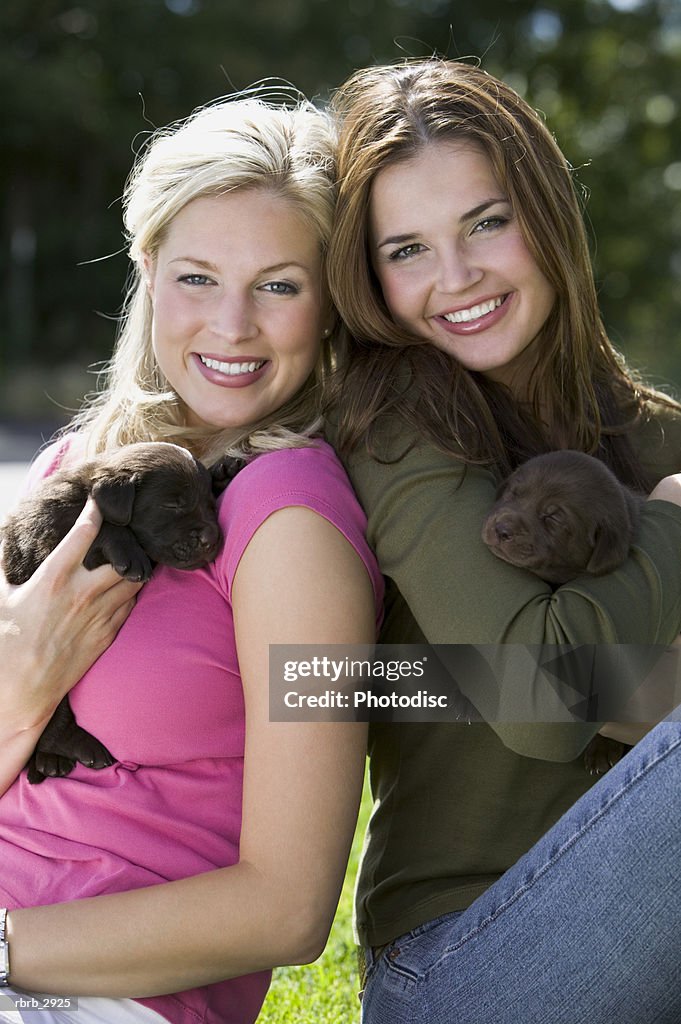 Portrait of two young women sitting holding two puppies