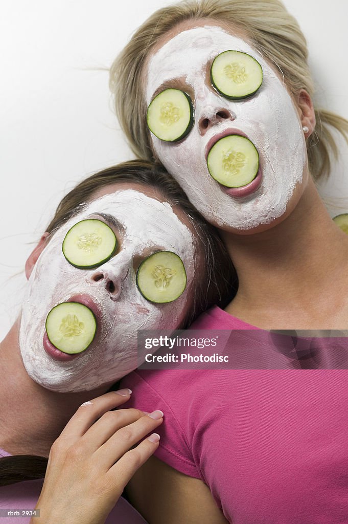 Two young women lying with facial masks and cucumber slices on their eyes and mouth
