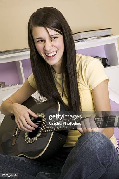 young woman playing an acoustic guitar smiling - plucking an instrument foto e immagini stock