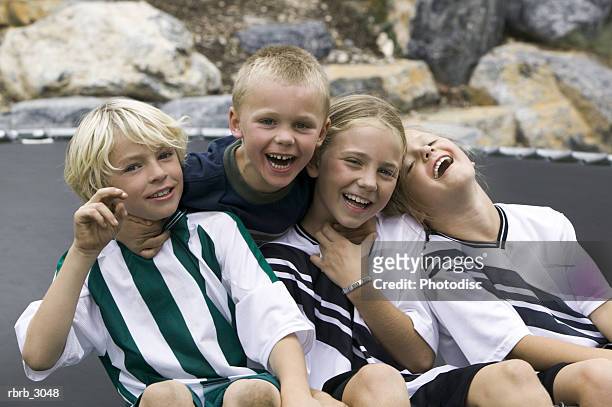 group of children sitting together smiling - front view portrait of four children sitting on rock stock pictures, royalty-free photos & images