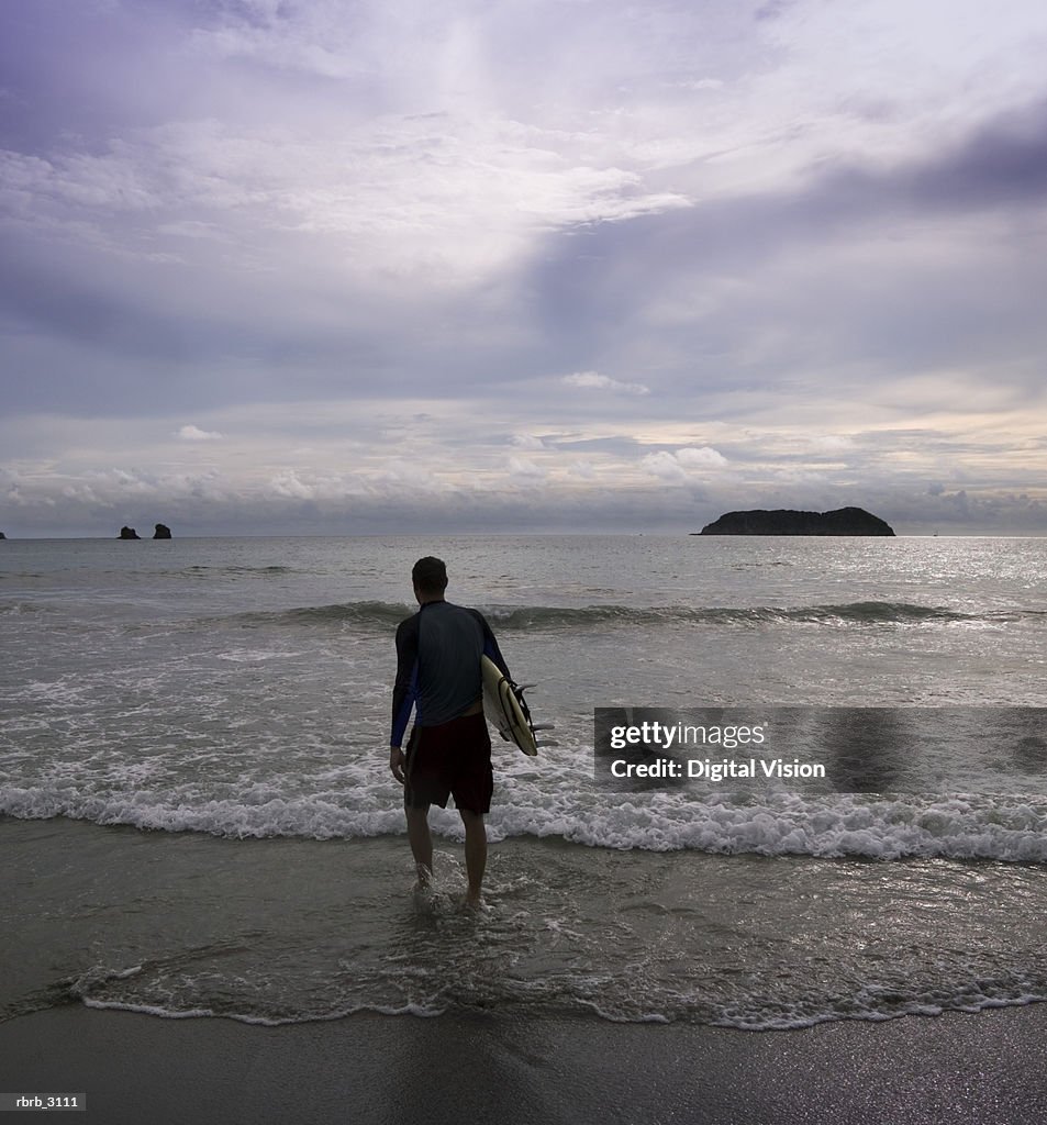 Rear view of a man with a surfboard walking towards the ocean