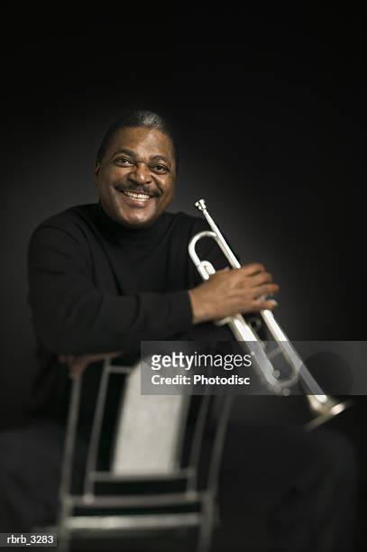 portrait of a man sitting on a chair holding a trumpet - bläser stock-fotos und bilder