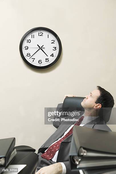 businessman sitting behind a desk looking at a wall clock - relógio de parede imagens e fotografias de stock