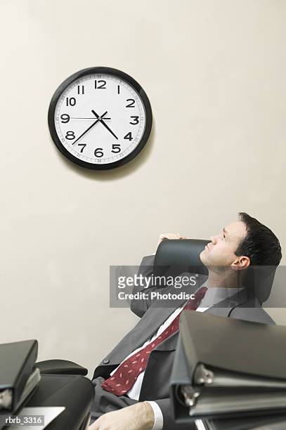 businessman sitting behind a desk looking at a wall clock - wall clock 個照片及圖片檔
