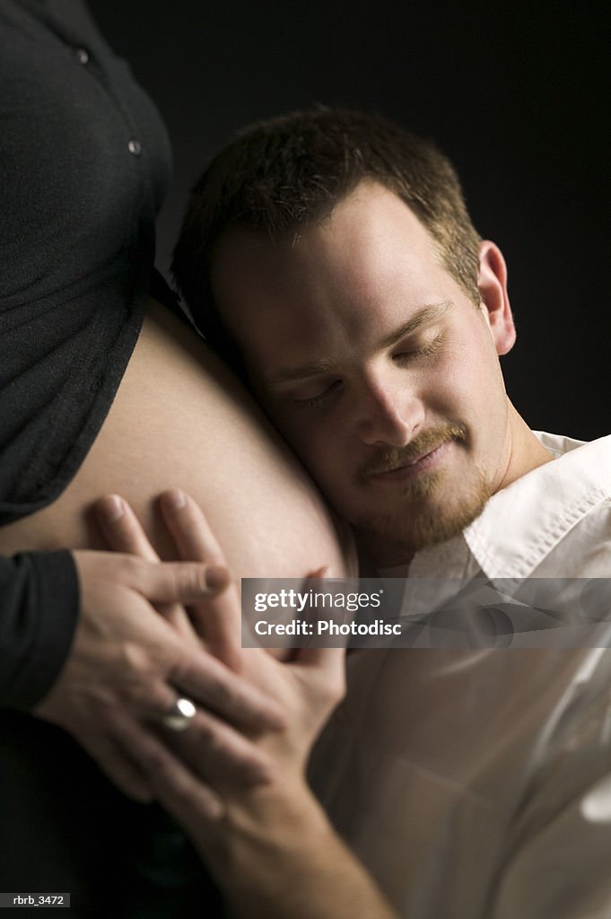 Mid adult man listening to a pregnant woman's stomach