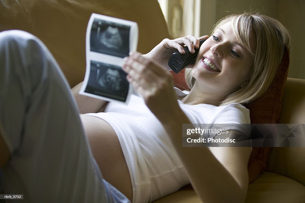 Young pregnant woman talking on a mobile phone holding an ultrasound