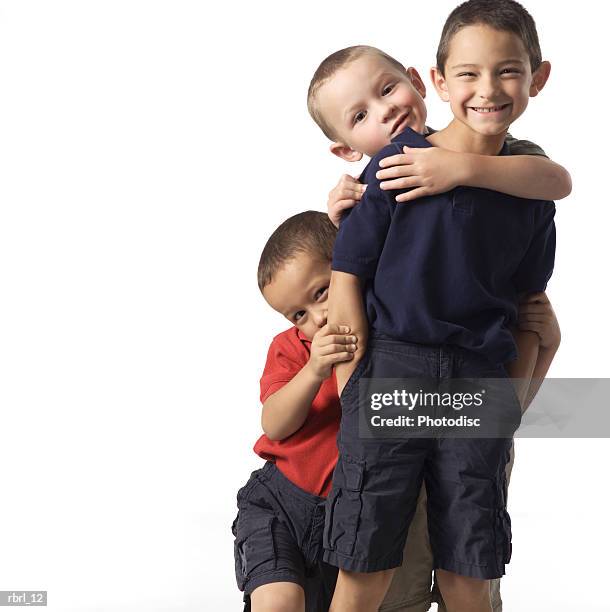 a group of three caucasian child brothers play and hug each other as they smile at the camera - smile stock-fotos und bilder