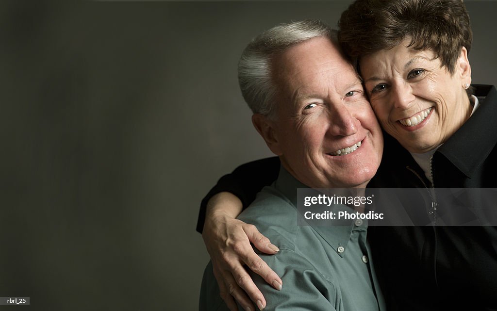 An elderly caucasian couple smile brightly as they hug each other