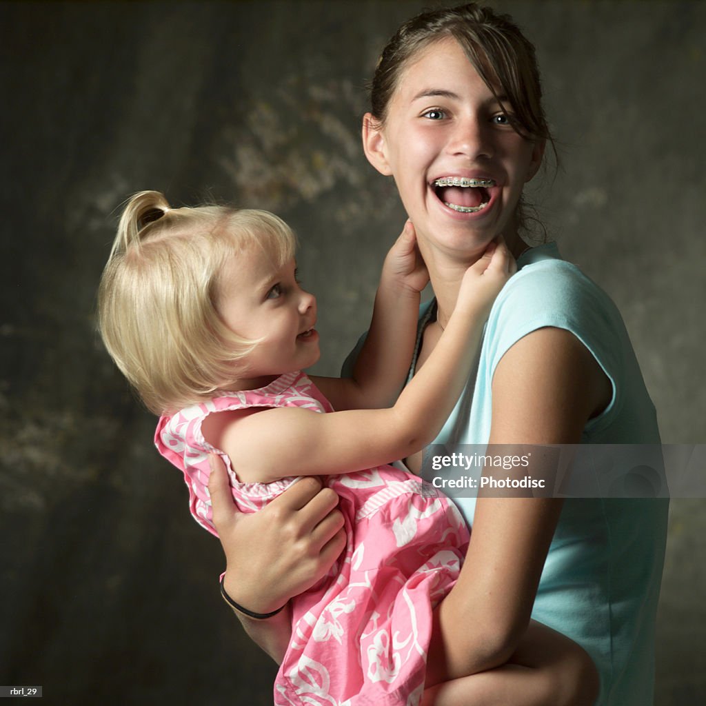 A young caucasian teenage girl laughs as she holds her little sister