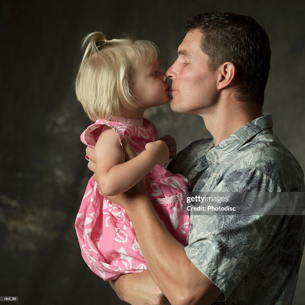 A caucasian father holds up and gives a kiss to his young daughter