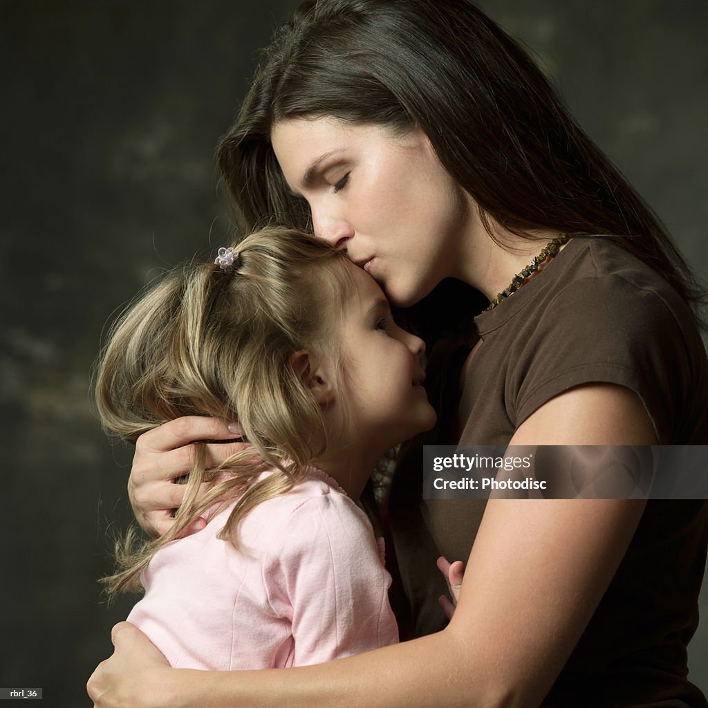 A young caucasian mother kisses the forehead of her young daughter on her lap
