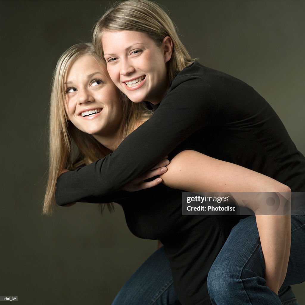 A caucasian blonde teenage girl carries her little sister on her back as they both smile