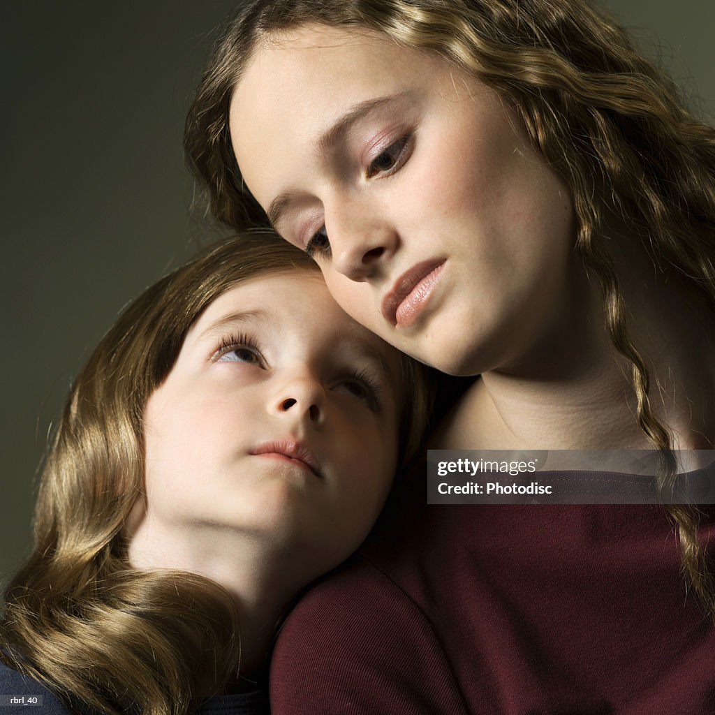 A caucasian teenage girl lovingly glances down at her little sister