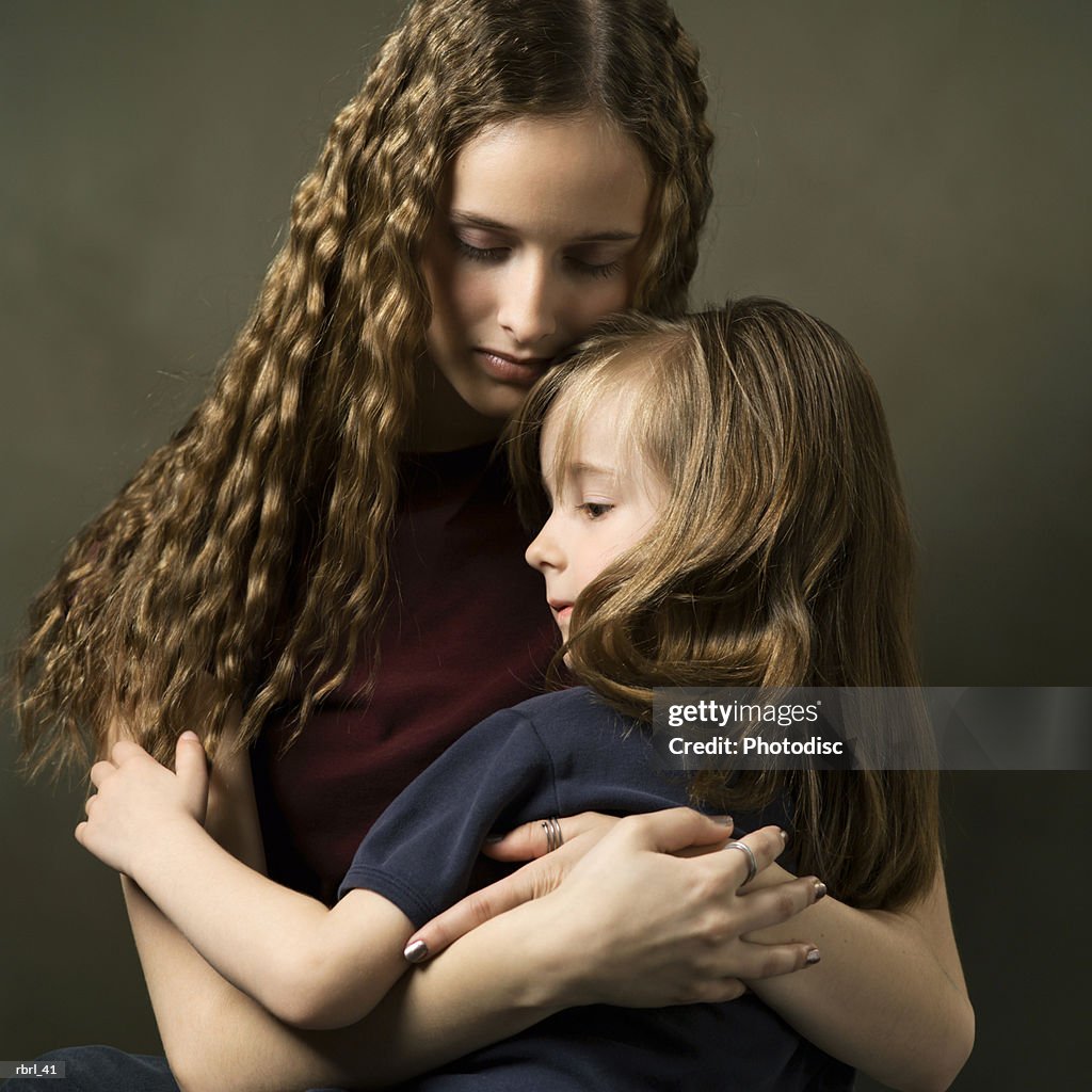 A caucasian teenage girl lovingly embraces her little sister