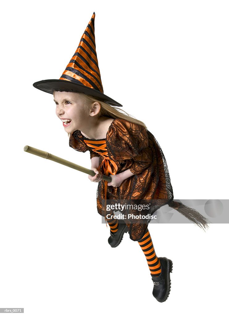 Full body shot of a female child dressed as a witch for halloween as she rides a broomstick