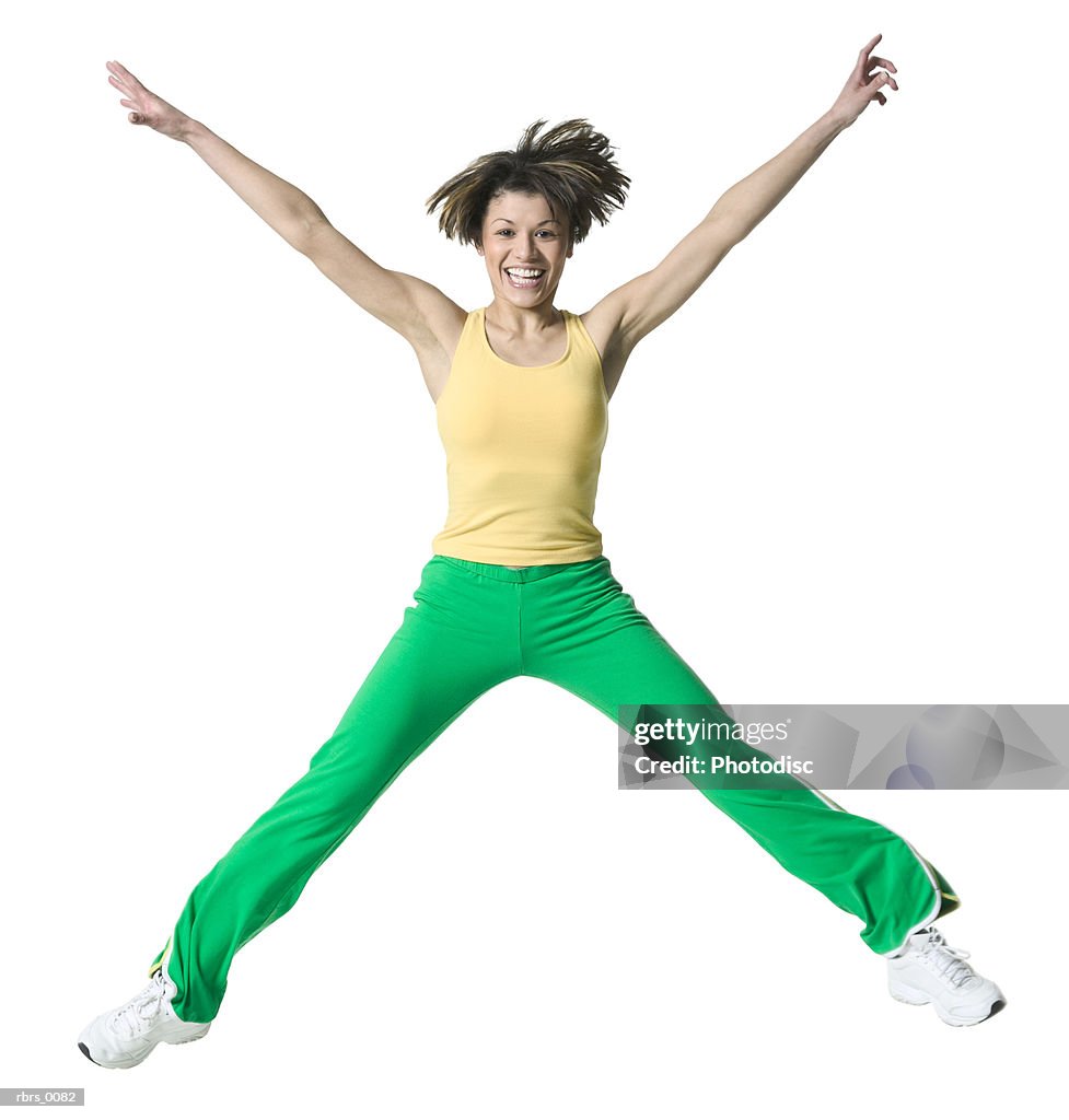 Full body shot of an adult woman in a workout outfit as she jumps up into the air