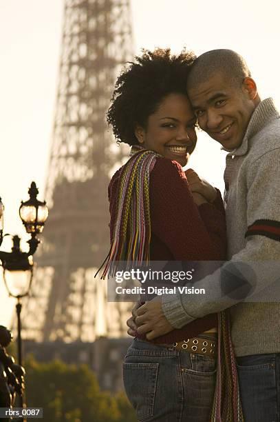 medium shot of a young adult couple as they embrace at the eiffel tower in paris and smile at the camera - smile bildbanksfoton och bilder