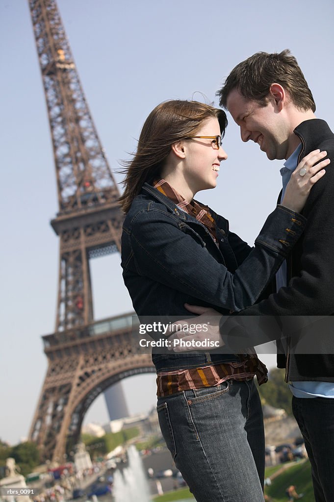 Medium shot of a young adult couple as they embrace at the eiffel tower in paris