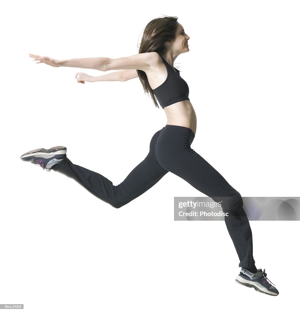 Full body shot of a young adult woman in a workout outfit as she jumps through the air