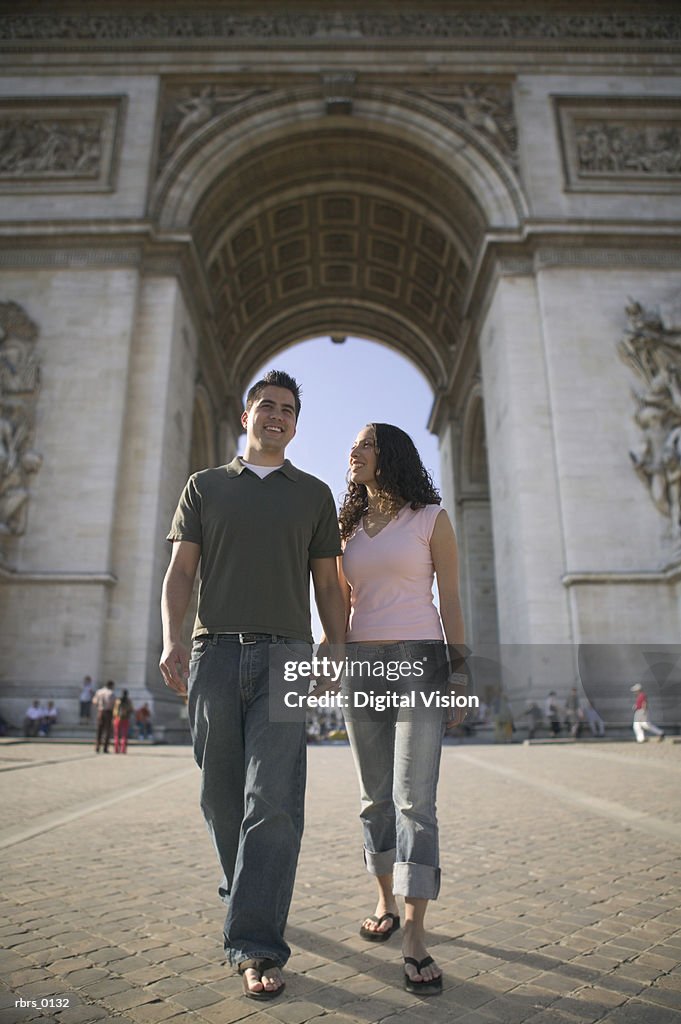 Wide shot of a young adult couple as they walk hand in hand while sightseeing in paris