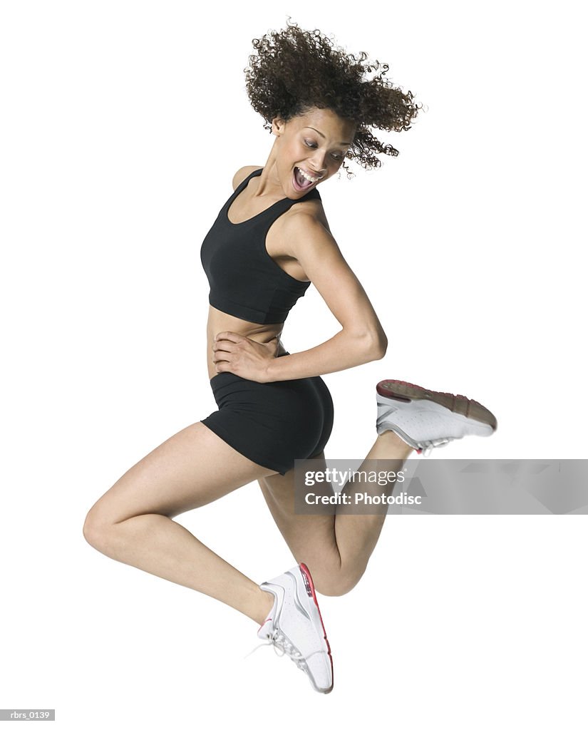 Full body shot of a young adult female in a workout outfit as she jumps through the air