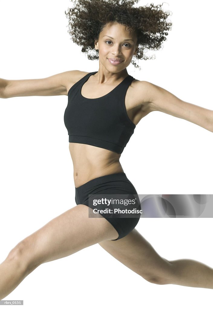 Medium shot of a young adult female in a workout outfit as she jumps through the air