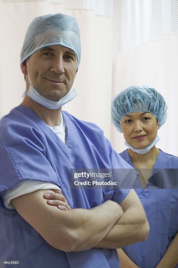 Medium shot of two adult medical surgeons as the pose in front of a curtain