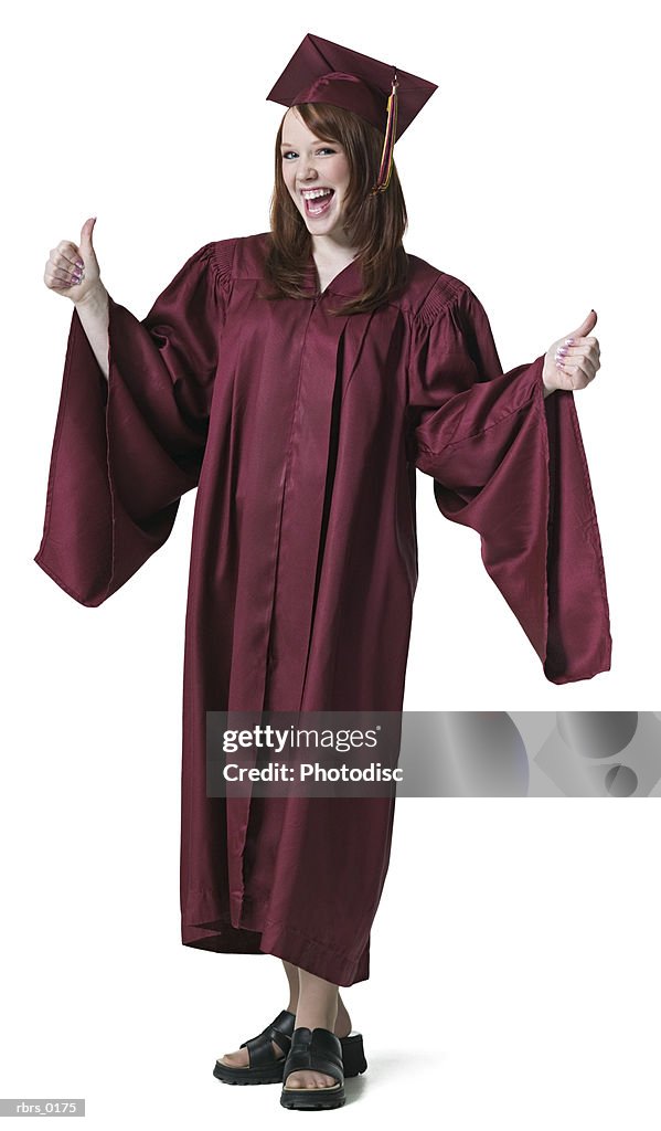 Full length portrait of a teenage female in her graduation cap and gown as she gives a thumbs up