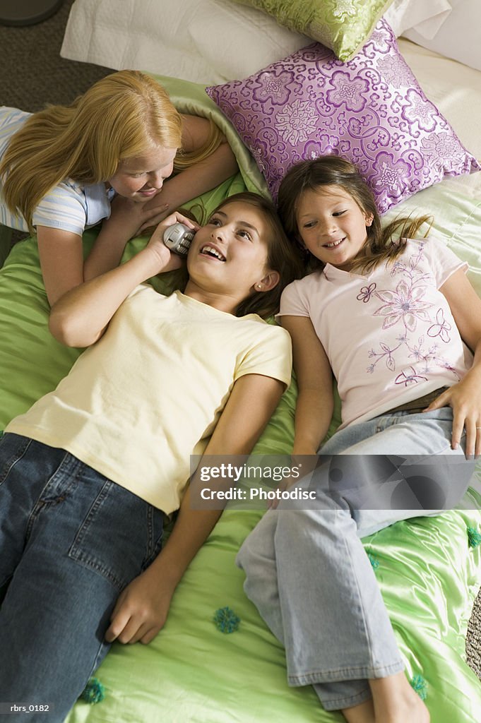 Lifestyle shot of three teenage girls as they lay on a bed and all chat on the phone