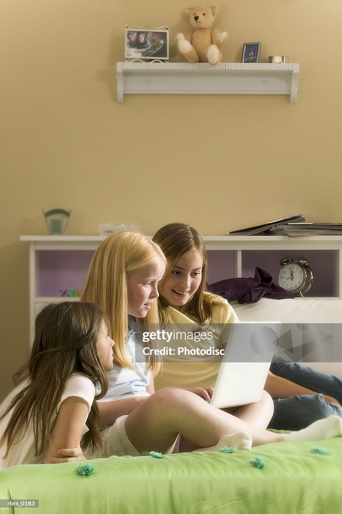 Lifestyle shot of three teenage girls as they sit on a bed and work on a laptop computer
