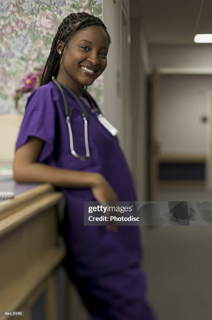 Lifestyle shot of a young adult female nurse with purple scrubs in a hospital hallway as she smiles