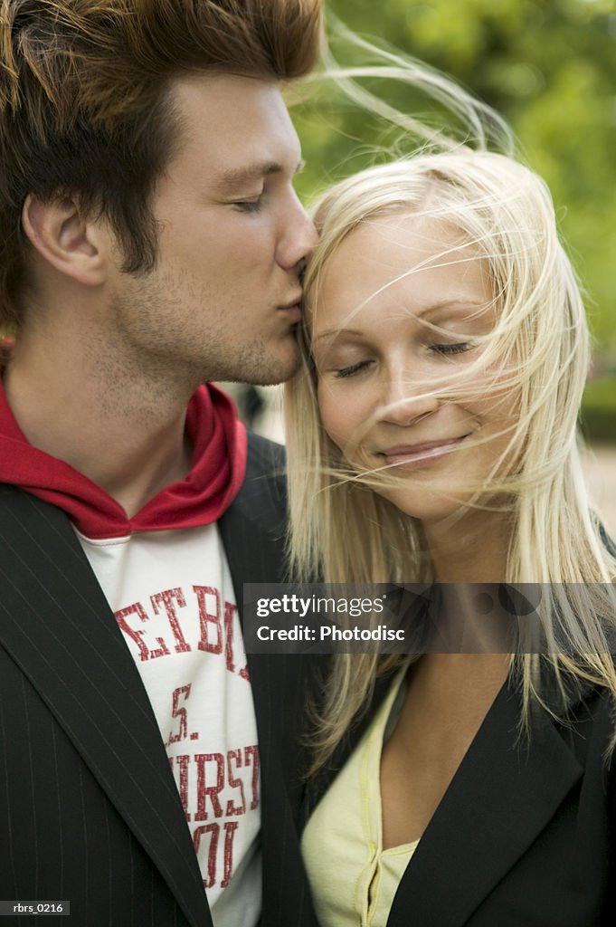 Lifestyle portrait of a young adult couple as the man leans in and kisses his girlfriend