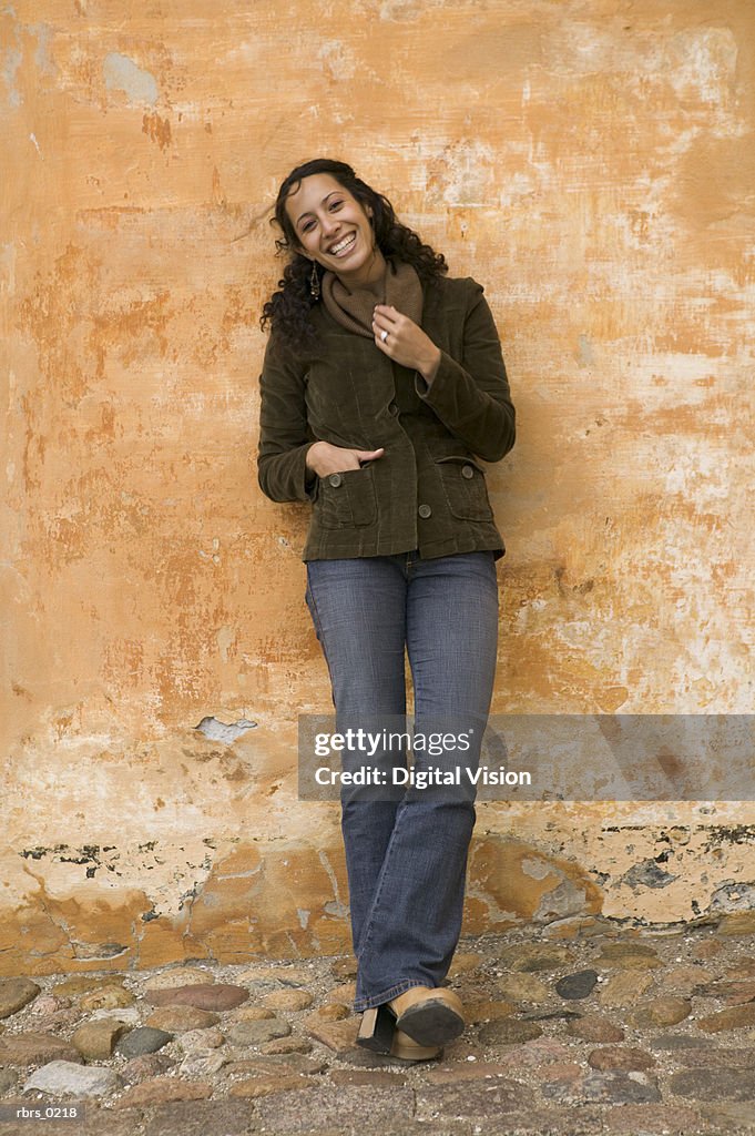 Lifestyle shot of an young adult female as she leans against an orange wall and smiles