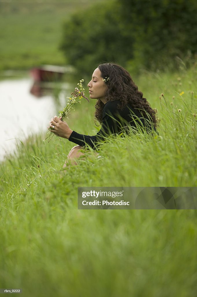 Lifestyle shot of an young adult female as she sits by a brook and picks wild flowers