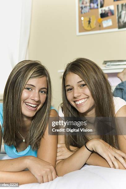 lifestyle portrait of two teenage girls as they lay on a bed and smile at the camera - smile bildbanksfoton och bilder