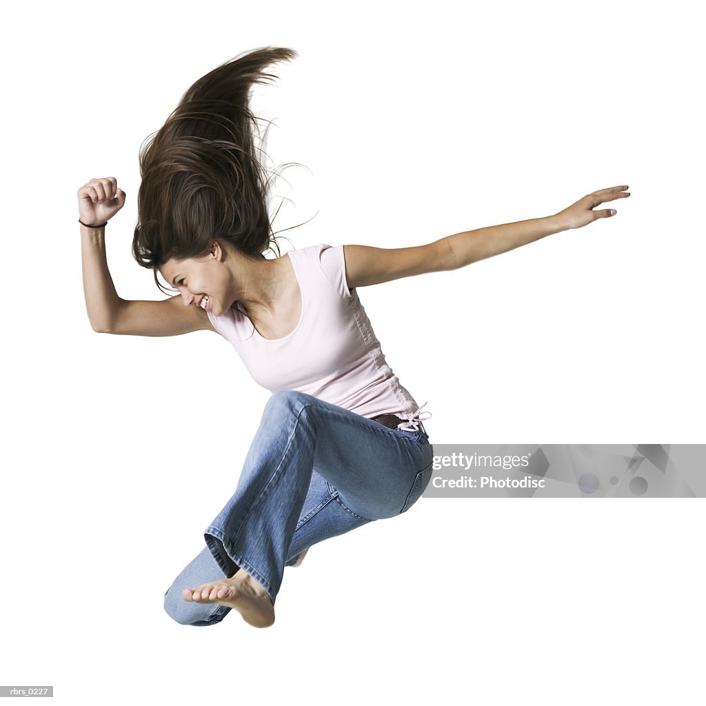 Full body portrait of a teenage female in jeans and a pink shirt as she jumps through the air