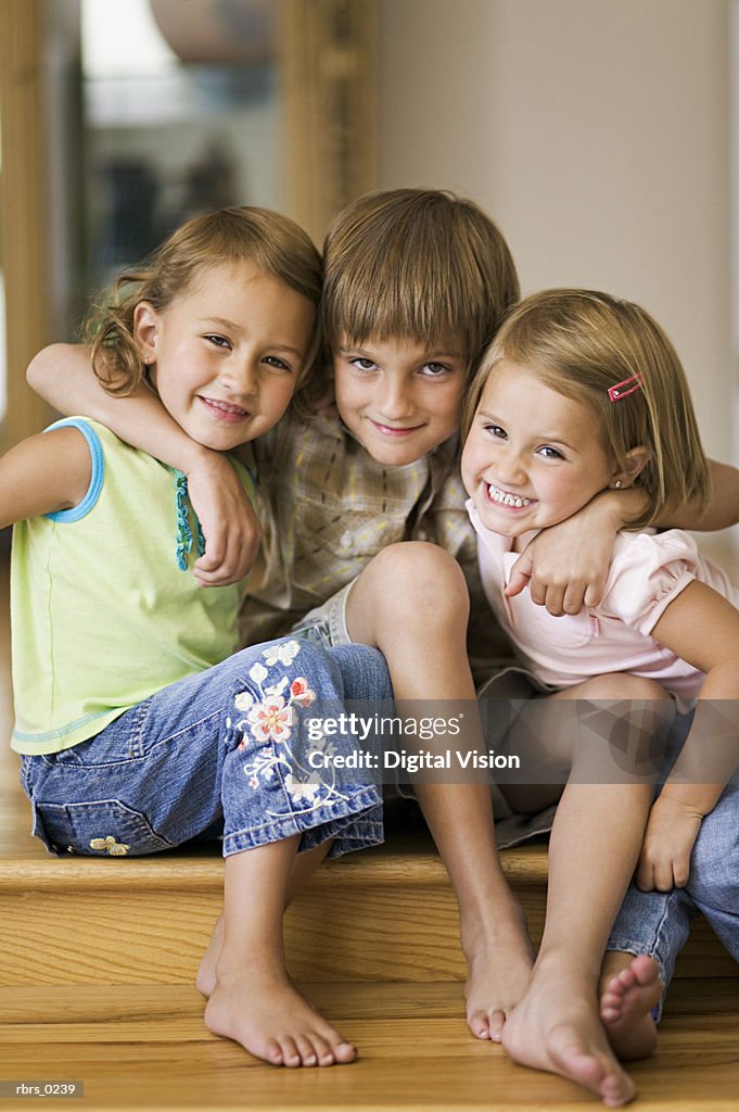 Lifestyle portrait of three siblings as they put their arms around each other and smile