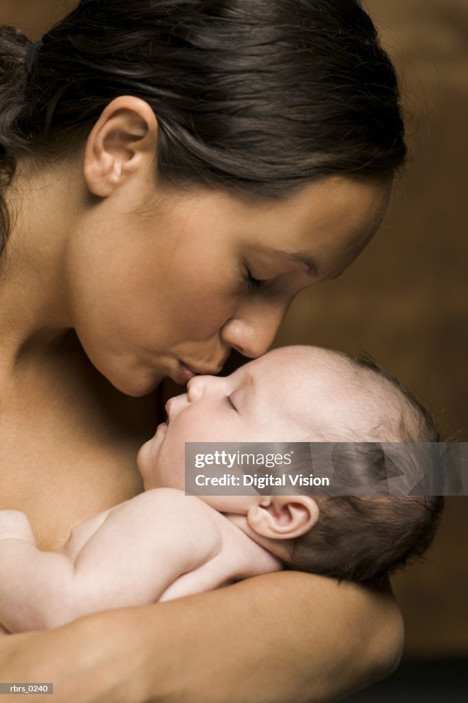 Relationship portrait of a young adult mother as she holds and kisses her newborn baby