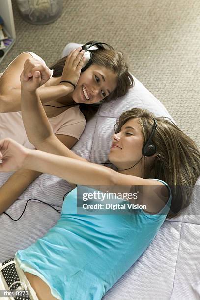 lifestyle shot of two teenage girls as they lay on a bed listening to music through headphones - bedroom radio bildbanksfoton och bilder