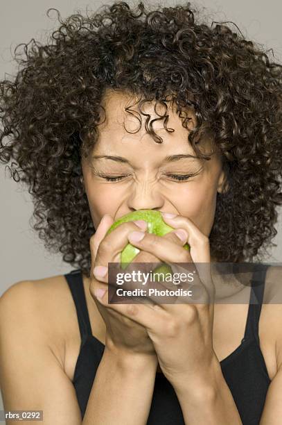 beauty portrait of a young adult female in a black tank top as she bites into an apple - black beauty stockfoto's en -beelden