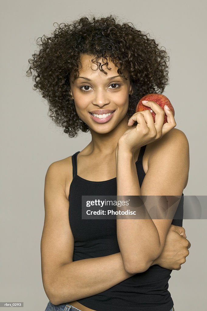 Beauty portrait of a young adult female in a black tank top as she holds up an apple