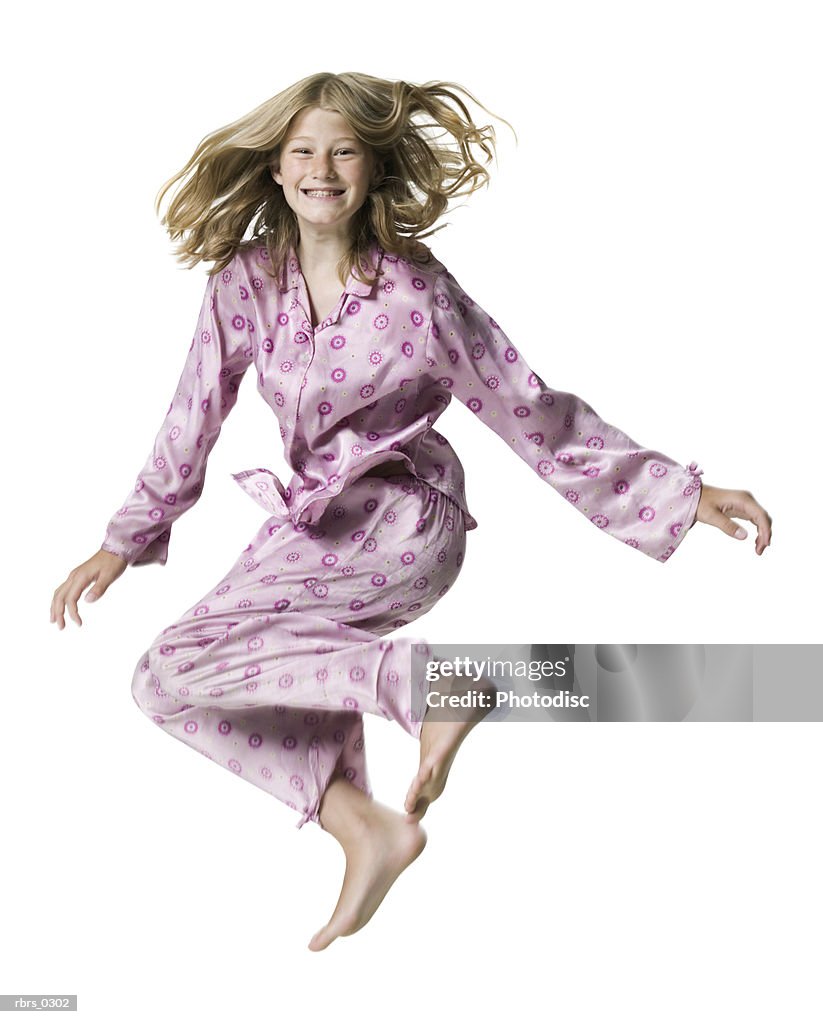 Full body portrait of a teenage female in pink pajamas as she jumps up in the air