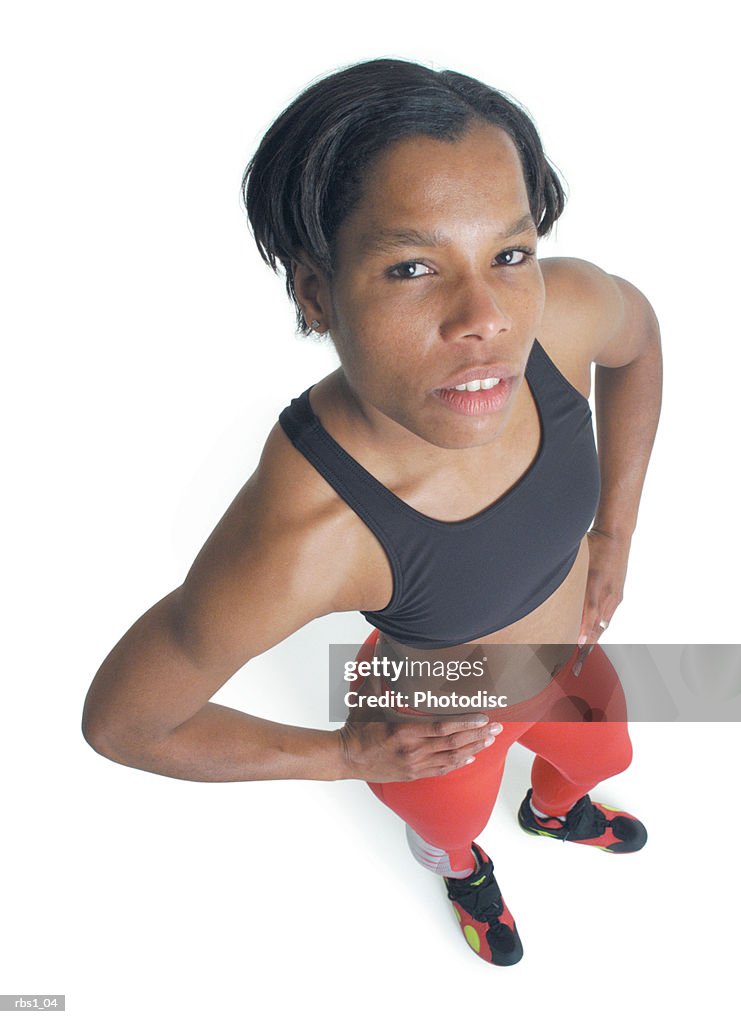 A young athletic black woman in red running pants is standing with hands on hips looking upward at the camera